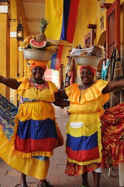 Smiling local fruit vendors in traditional dress carrying baskets on their heads
